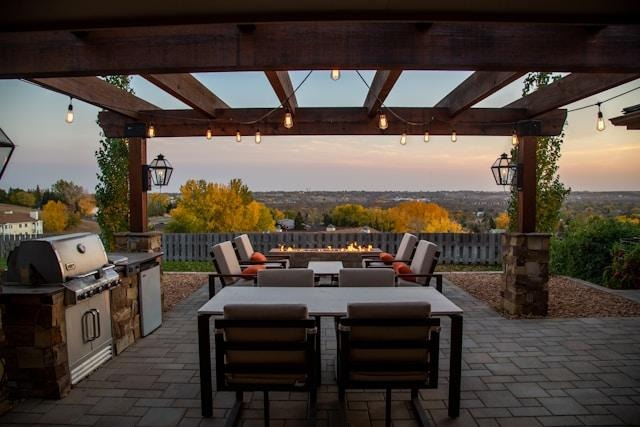 image - Lead Grow Develop - Business, Technology, Personal Development Outdoor patio dining area under a wooden pergola with string lights, a long gray table and cushioned chairs, sunset hillside view.