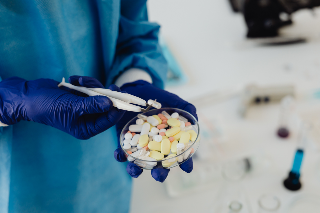 image - Lead Grow Develop - Business, Technology, Personal Development Gloved hands holding a bowl of assorted pills in a clinical setting.