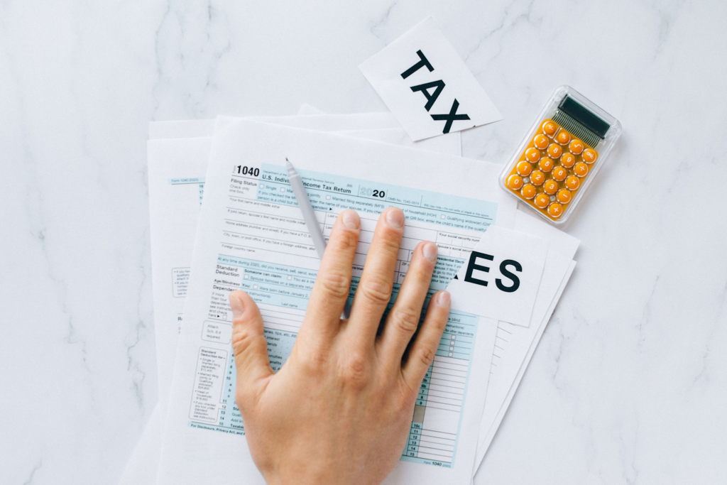 image - Lead Grow Develop - Business, Technology, Personal Development Hands filling out a Form 1040 tax return on a light surface with an orange calculator nearby