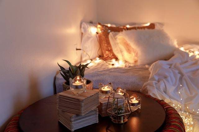image - Lead Grow Develop - Business, Technology, Personal Development Cozy bedroom scene with a bed, warm string lights, and a round table holding candles, a plant, and a stack of napkins.