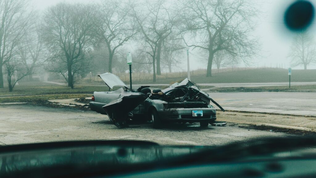image - Lead Grow Develop - Business, Technology, Personal Development Wrecked gray sedan in a foggy parking lot, with crumpled metal and debris around it, bare trees in the background.