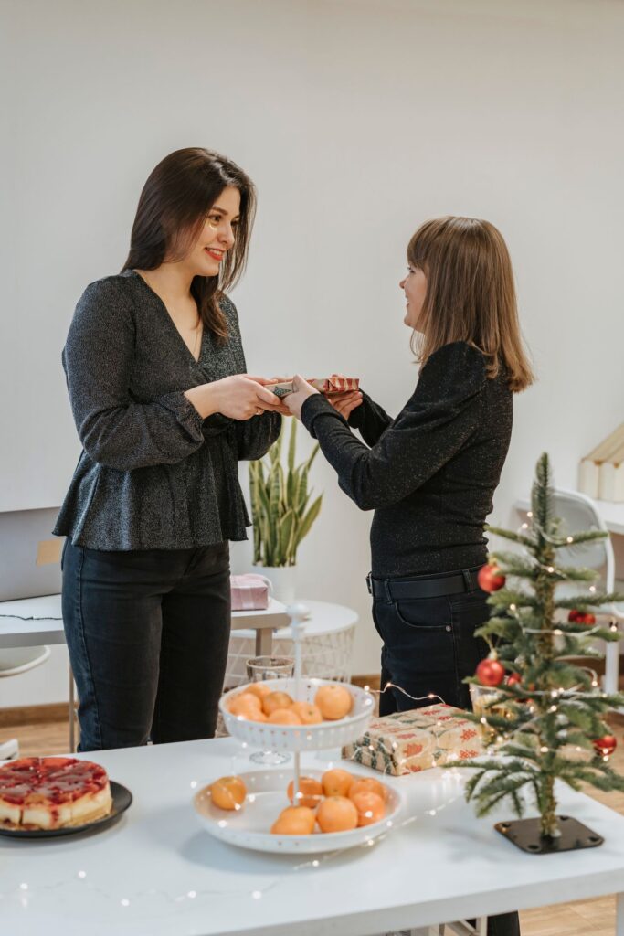 Two women exchanging gifts during a festive Christmas celebration indoors with holiday decor