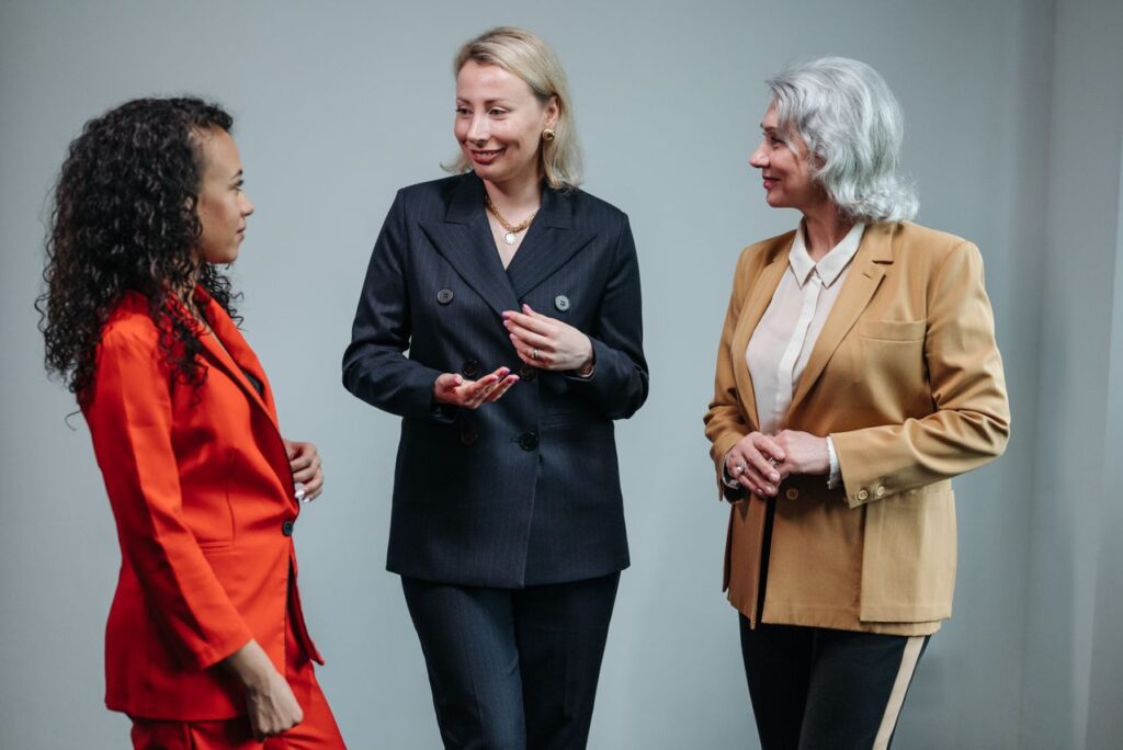 pexels-pavel-danilyuk-8424894 - Lead Grow Develop - Business, Technology, Personal Development Three women in business attire having a conversation indoors, showcasing diversity and teamwork