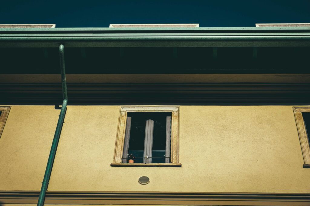 A beige building facade with windows and a drainpipe, captured from a low angle outdoors.