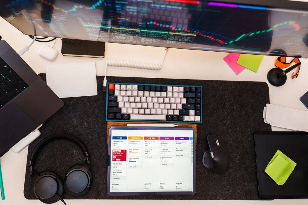 Top view of a tech workspace featuring a digital tablet, keyboard, monitor, and headphones for project management